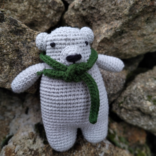 Ourson en crochet mignon avec écharpe verte, entouré de pierres naturelles.